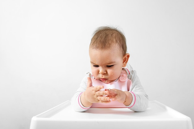 Happy baby toddler in high chair with spoon in his hand