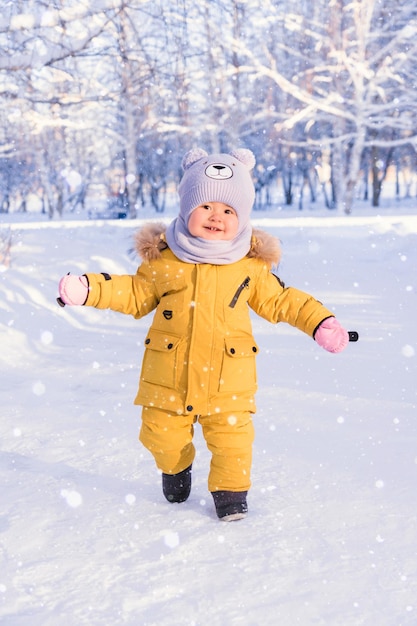 A happy baby in winter clothes enjoys the snow while walking in a winter park