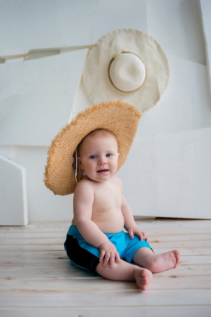 Happy babyjongen in blauwe korte broek en een strooien hoed op een wit oppervlak met ruimte voor tekst