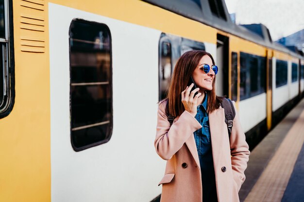 Фото Счастливая белая женщина на платформе на железнодорожном вокзале разговаривает по мобильному телефону.