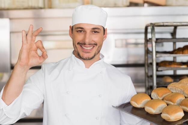 Foto panettiere felice che mostra vassoio di pane fresco