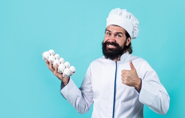 Happy baking perfect eggs quality concept of housekeeping mature bearded man wear chef hat male cook ready for preparing food brutal hipster in apron going to be cooking meal time for eating