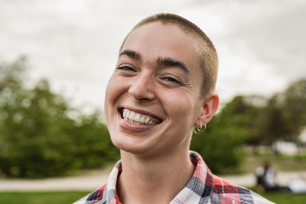 Felice ragazza calva sorridente sulla fotocamera al parco cittadino