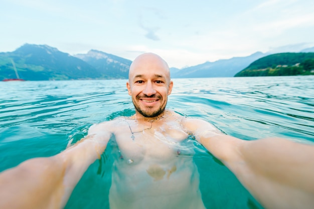 Happy bald man standing in lake and taking selfie