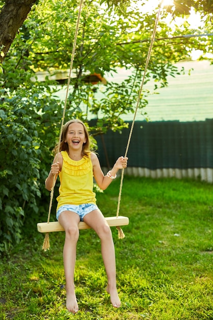 Happy barefoot laughing child girl swinging on a swing in sunset summer day