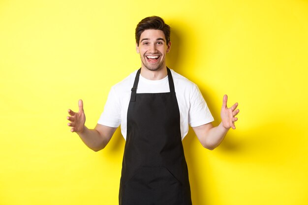 Happy barista holding something big shaping large object standing over yellow background