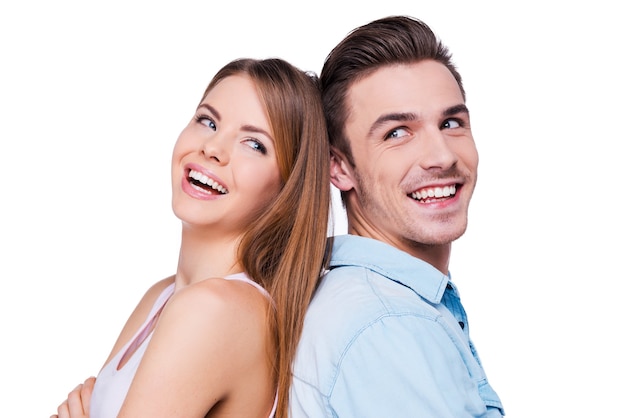 Happy to be together. Beautiful young loving couple smiling and standing back to back against white background