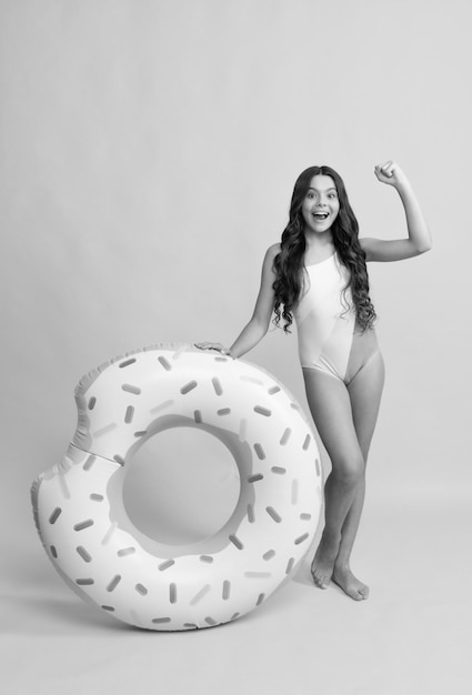 Happy beach kid in swimsuit with doughnut inflatable ring on yellow background summer vacation