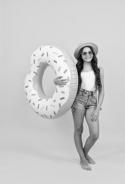 Happy beach kid with curly hair in straw hat and sunglasses with doughnut inflatable ring for pool party fun on summer vacation on yellow background summer vacation