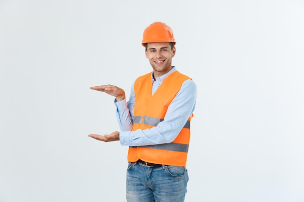 Happy beard engineer holding hand on side and explaining something guy wearing caro shirt and jeans with yellow vest and orange helmet isolated on white background