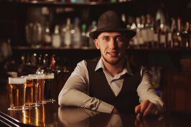 Happy bearded bartender at bar counter with glasses of beer