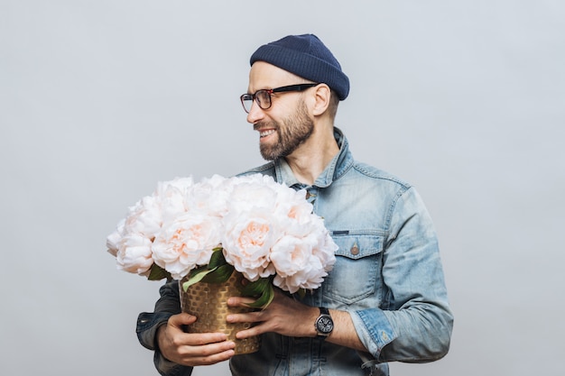 happy bearded male looks away while holds bunch of white flowers