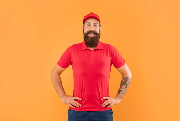 캐주얼 빨간 모자와 문신된 팔 akimbo 노란색 배경 남자와 서 있는 tshirt에서 행복 한 수염된 남자