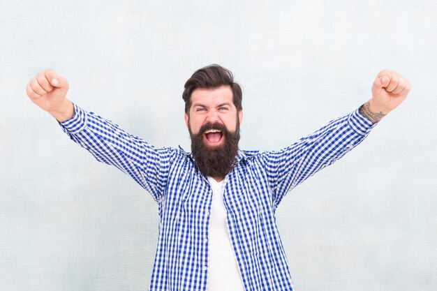 Happy bearded man celebrate victory keeping arms upward fingers clenched winning gestue blue background winner