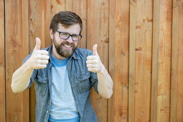 A happy bearded man in glasses gestures show thumbs up on two hands and smiling looks