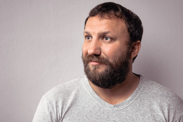 Happy bearded man in gray t-shirt looking away while standing against gray wall.