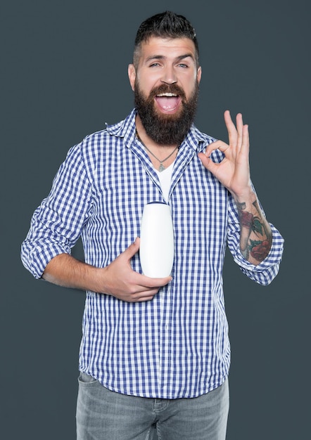 Happy bearded man hold beauty product of aftershave bottle\
ok