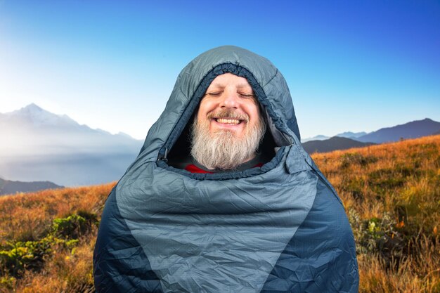 写真 山の自然を背景にしたスリーピングバッグの幸せなひげの男