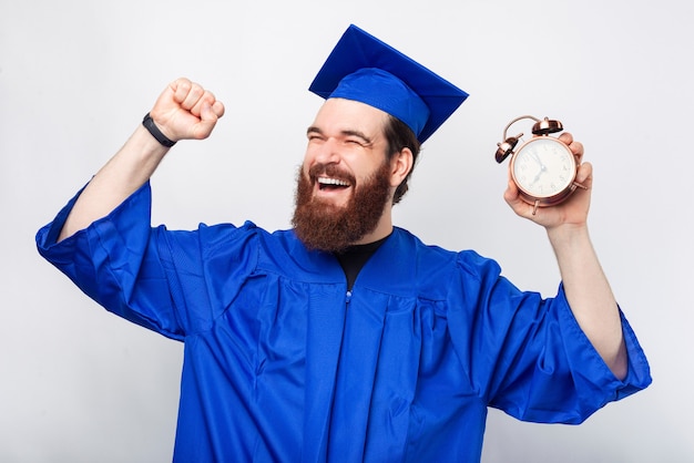 Happy bearded man is making the winner gesture while he is holding an alarm clock.