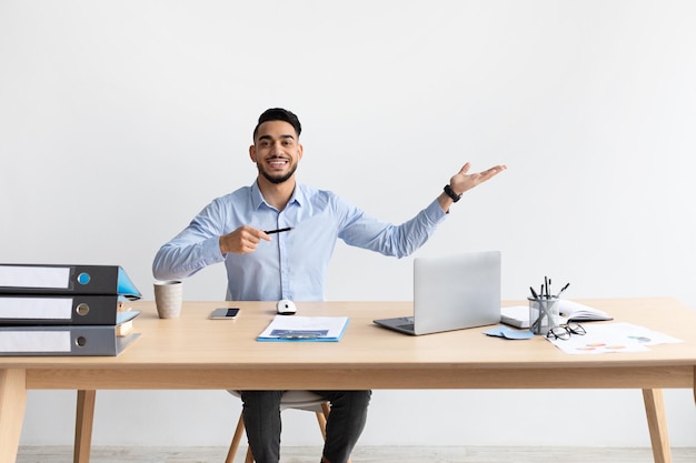 Happy bearded man pointing aside sitting at workplace