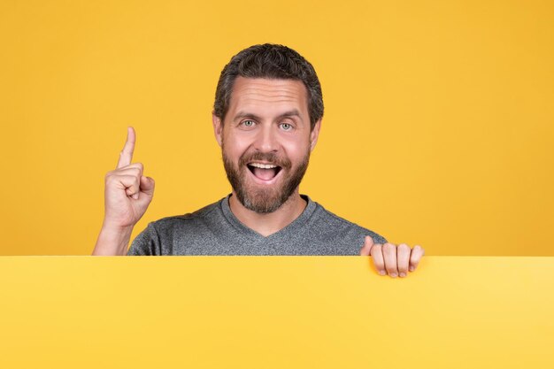 happy bearded man raised finger inspired with idea behind yellow paper for copy space, advertisement.