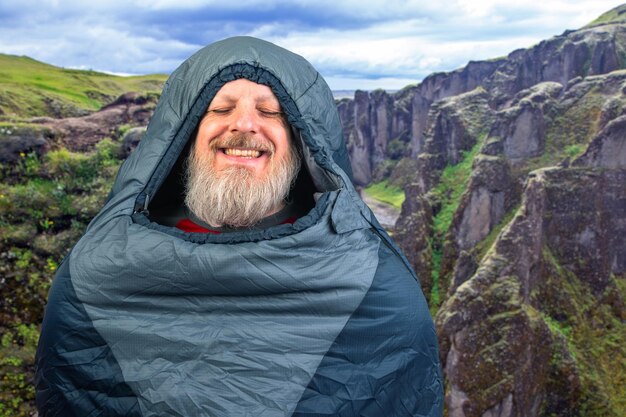 Photo happy bearded man in a sleeping bag against the backdrop of nature in the mountains nature hikes