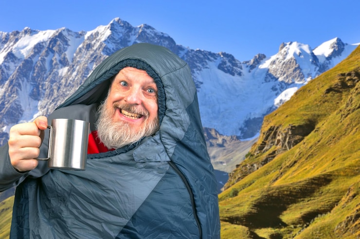 Photo happy bearded man in a sleeping bag with a cup of coffee against the backdrop of nature