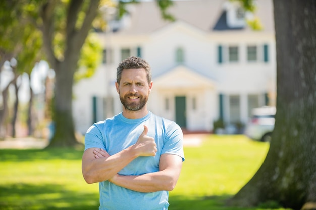 Happy bearded man standing showing thumb upon house background broker