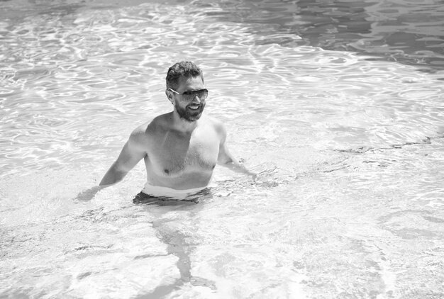 Happy bearded man in sunglasses swimming in pool water on summer vacation summertime