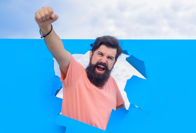 Happy bearded man through hole in blue paper win through paper advertising happy emotions smiling