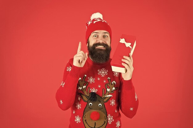 Happy bearded man wearing funny knitted sweater and santa claus hat and hold present box has an idea for celebrating new year party new year shopping