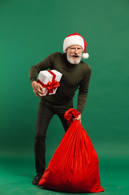 Happy bearded modern Santa Claus holding gift box and red sack