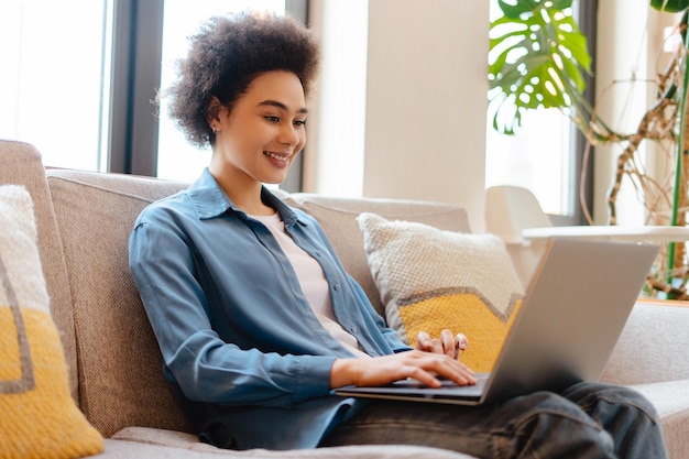 Happy beautiful African American woman freelancer using laptop watching video checking email