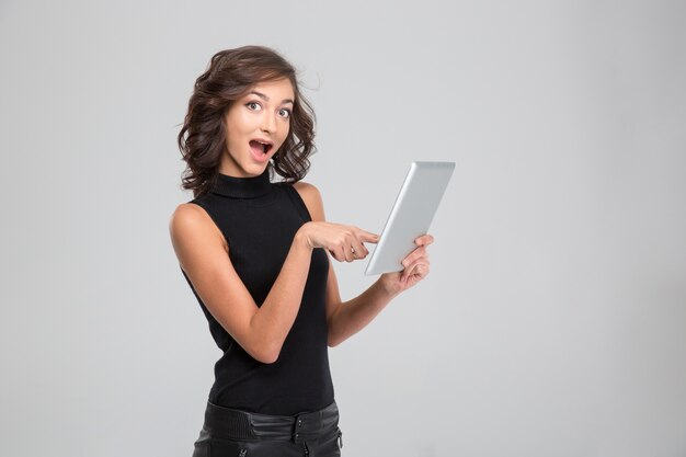 Happy beautiful amazed young woman pointing on tablet