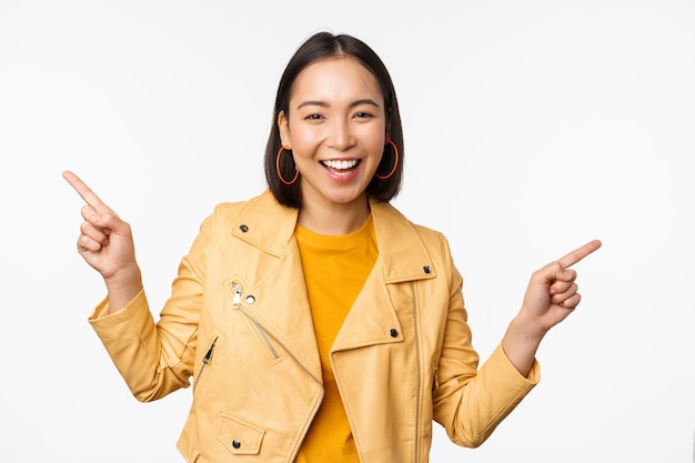 白い背景の上に黄色のジャケットで立っている販売を示すバナーのロゴを示す左と右の指を指す幸せな美しいアジアの女の子