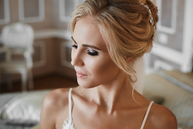 Happy and beautiful blonde model girl with perfect makeup and with stylish wedding hairstyle decorated with jewelry