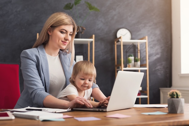 Photo happy beautiful business mom working on laptop in office while spending time with her cute baby. business, motherhood, multitasking and family concept.