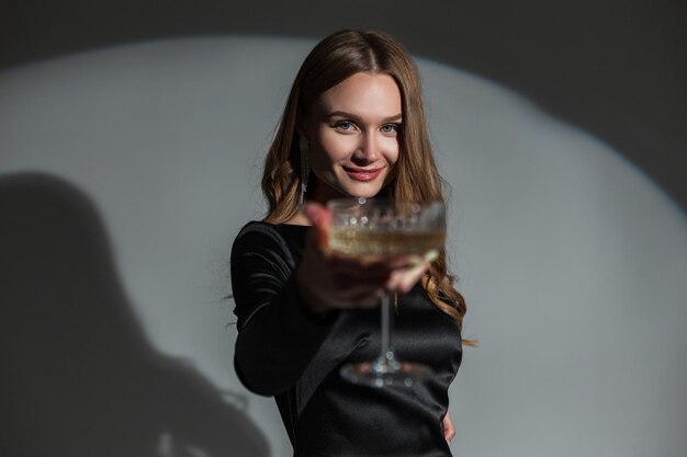 Happy beautiful chic woman with a smile in a fashionable elegant black dress holding a vintage glass of champagne at a party Pretty lady celebration