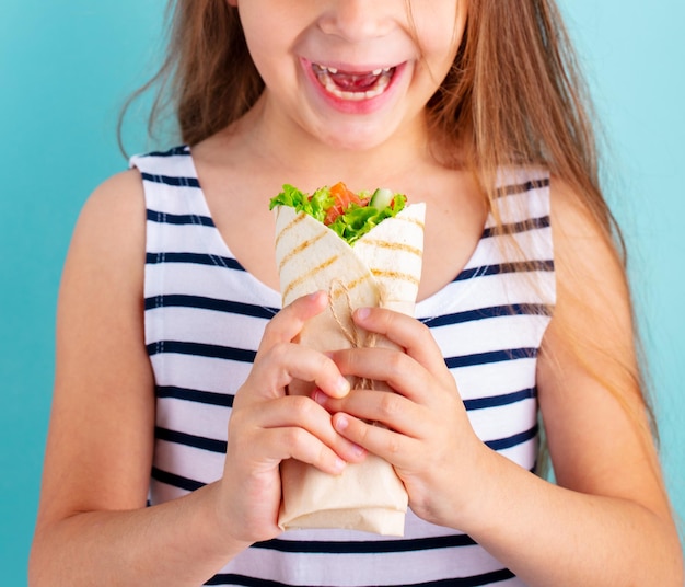 ラップ サンドイッチを食べて幸せな美しい子供女の子青色の背景をクローズ アップ