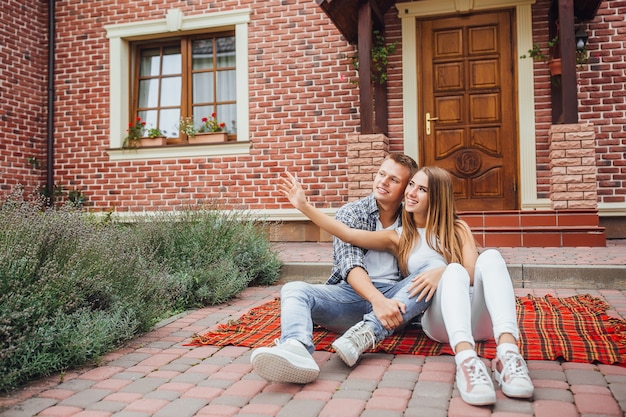 Happy beautiful couple sitting at the blanket  carpet in front of the new home