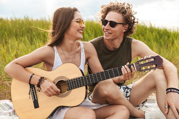 Happy beautiful couple sitting at the park together, playing guitar, relaxing