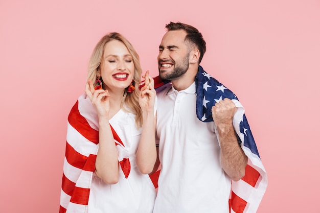 Photo happy beautiful couple standing isolated over pink , carrying american flag, celebrating