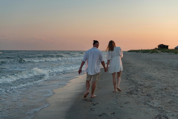 Happy beautiful couple walking at sunset along the seashore