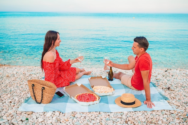 Bella famiglia felice su una spiaggia tropicale che ha picnic insieme sul tramonto