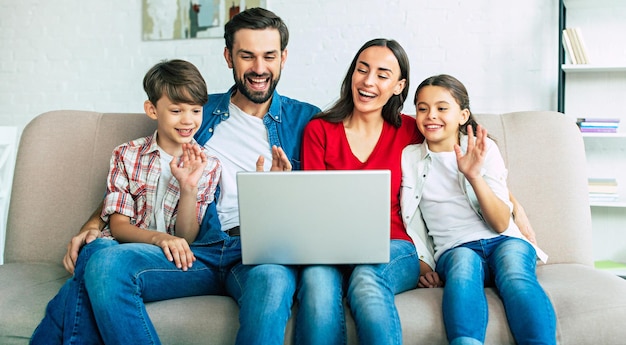 カジュアルな服装で自宅のソファにノートパソコンで幸せな美しい家族
