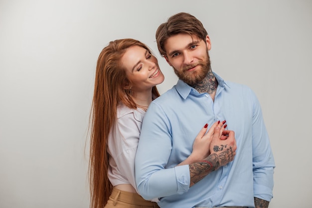 Happy beautiful fashionable young couple in the studio Beautiful happiness redhead girl and handsome hipster guy with tattoo and beard in elegant clothes