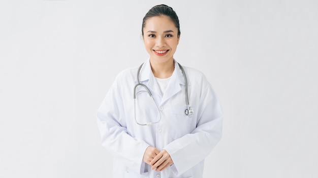 幸せな美しい女性医師は医師のコートを着て十字架の腕で白に隔離して立っています
