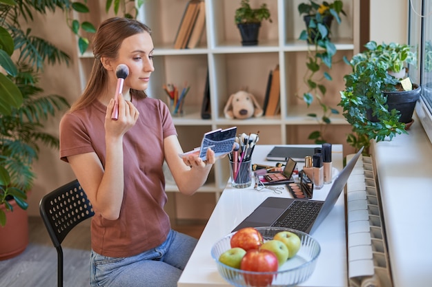 Happy beautiful female doing makeup while studying online at home