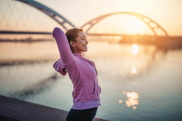 Happy beautiful female jogger exercising next to river.