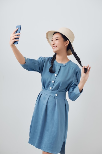 Happy beautiful girl in casual or hipster style pigtail hairstyle standing holding mobile smart phone and doing selfie